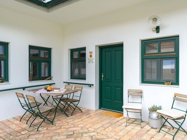 Eine Terrasse mit Tisch und Stühlen, eine grüne Tür und Fenster mit grünen Rahmen.