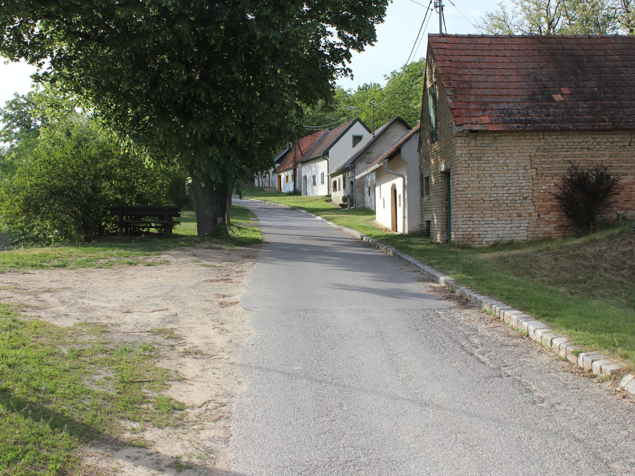A quiet street lined with traditional brick houses, a gravel path, and a bench.