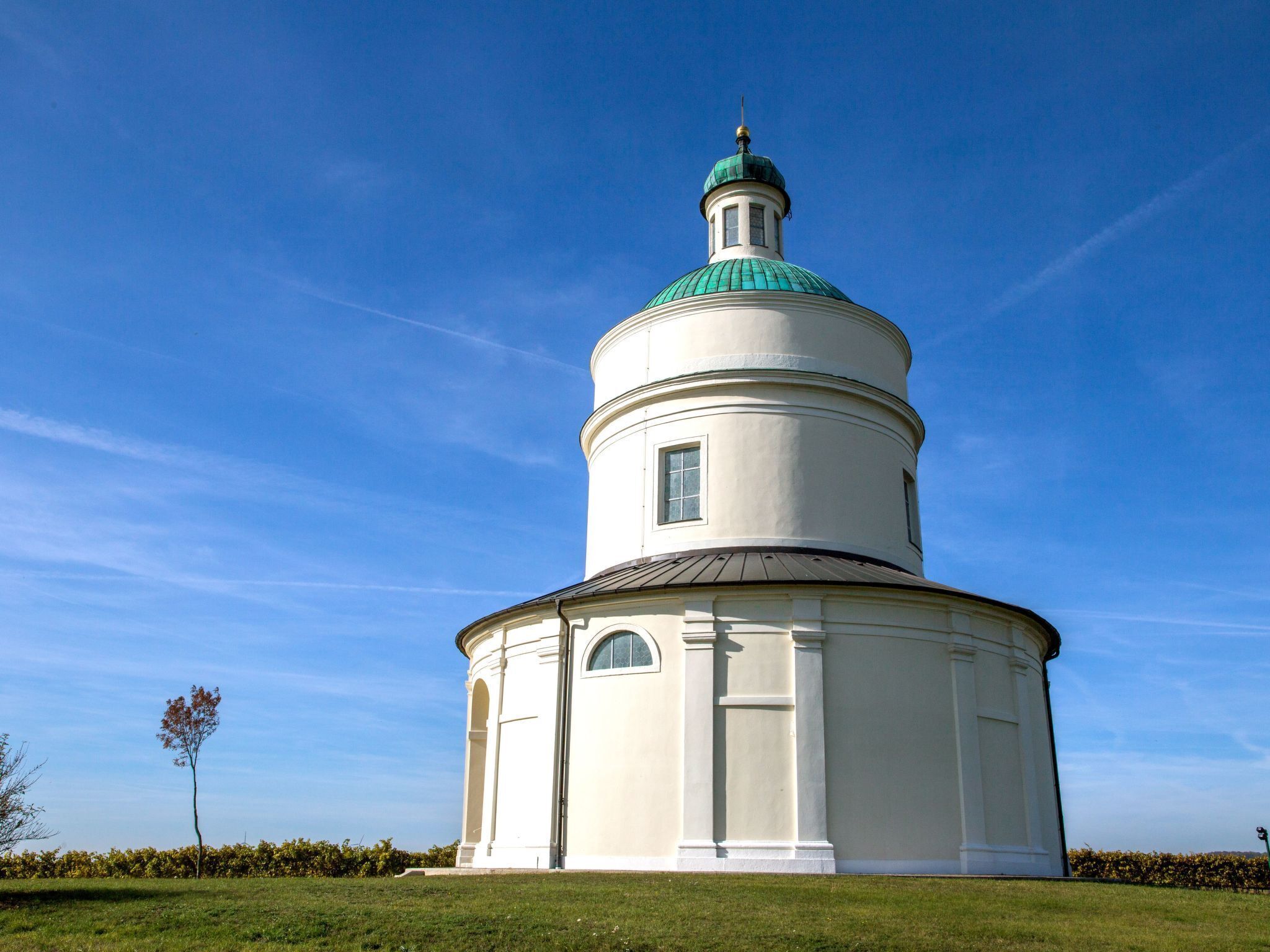 Ein weißes, rundes Gebäude mit einer grünen Kuppel und einem kleinen Turm, umgeben von einer Rasenfläche.