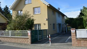 Un immeuble résidentiel de deux étages, à la façade beige, doté d’une antenne parabolique et d’une entrée fermée par un portail.