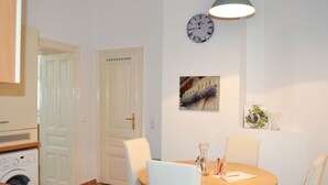 Ein Essbereich mit einem runden Tisch, weißen Stühlen, einer Wanduhr und einer Pendelleuchte.