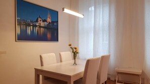 Un comedor con una mesa, sillas, un jarrón con flores y un cuadro de un paisaje urbano en la pared.