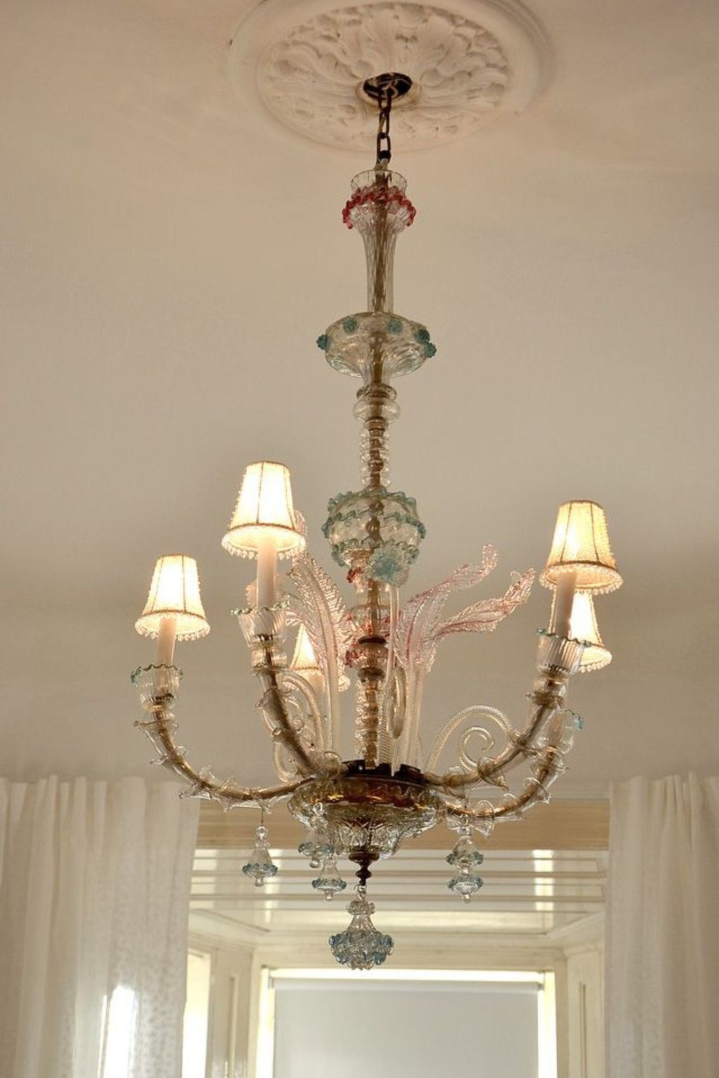 A chandelier with multiple arms and lampshades, hanging from a ceiling with a decorative pattern.