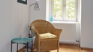 Huoneessa on rottinkituoli, pieni lasitasoinen pöytä, lattiavalaisin ja ikkuna, josta avautuu näkymä puihin.
