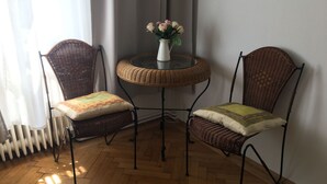 Een hoek van een kamer met twee rieten stoelen, een klein rond tafeltje en een bloemenvaas, plus een radiator.