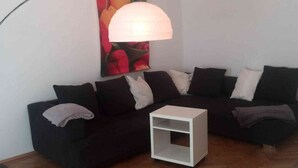 Een woonkamer met een zwarte modulaire bank, een witte bijzettafel en een vloerlamp.