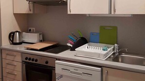 Et kompakt køkken med komfur, ovn, opvaskemaskine og en bordplade med brødrister og elkedel.