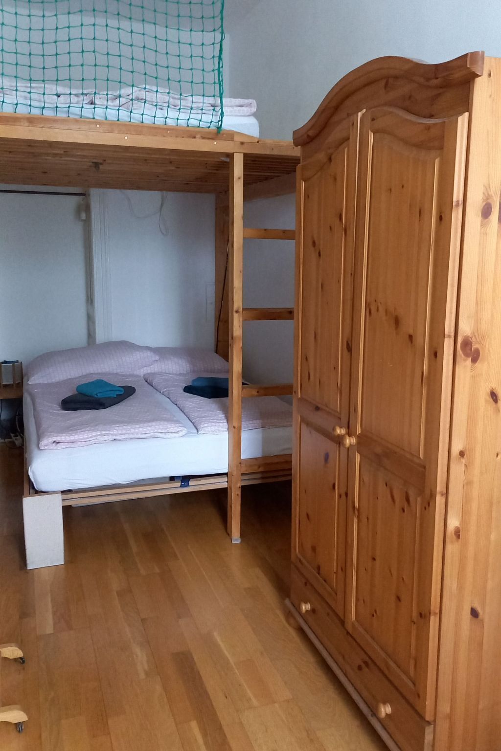 A bunk bed with a wooden ladder, a wardrobe, and a netted area above the bed.