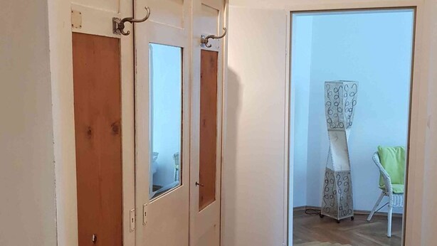 En gang med trægulv, der fører til et værelse med en stor garderobe og et spejl.