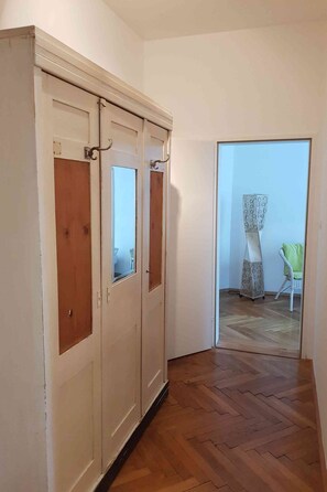Een hal met een houten vloer die leidt naar een kamer met een grote garderobe en een spiegel.