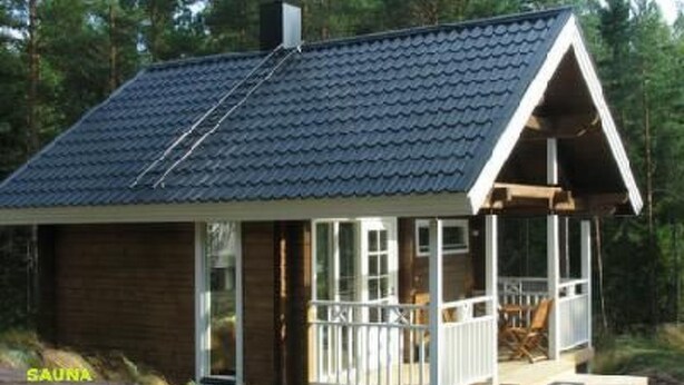 A wooden cabin with a sloped roof, large windows, and a porch with chairs.