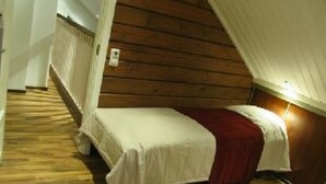A small, cozy room with a wooden sloped ceiling, a single bed with a white bedspread and a red blanket, and a white radiator on the wall.