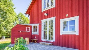 Ein rotes Holzhaus mit einer Holzdiele, einem kleinen Tisch und einer Sitzbank.