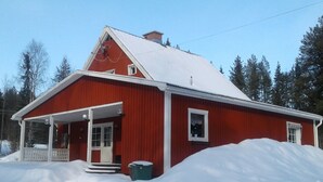 Una casa de madera roja con techo nevado y un porche.