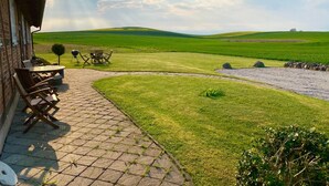 Eine Terrasse mit Gartenmöbeln, ein Steinweg und Blick auf ein grünes Feld und Hügel.
