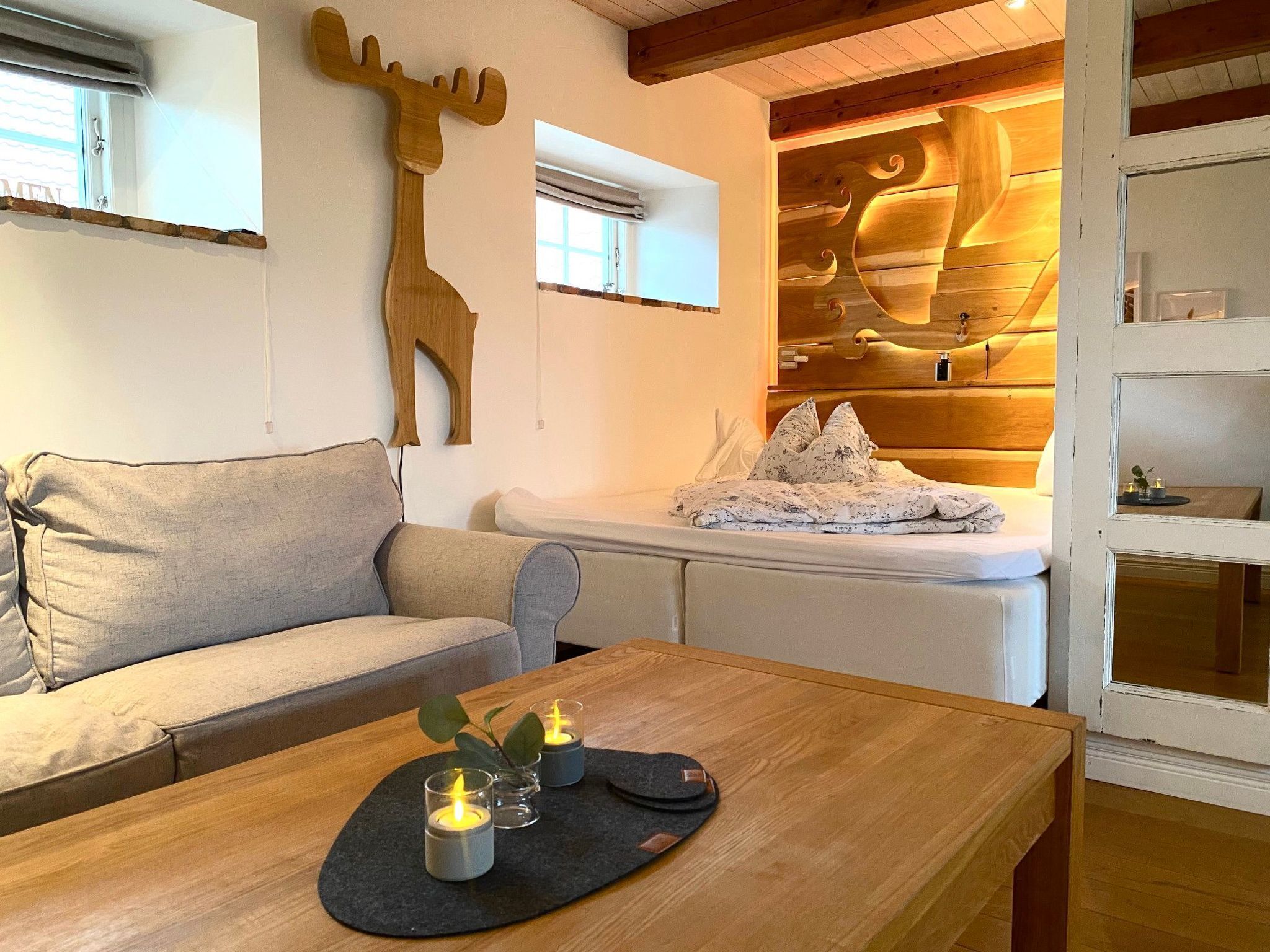 Een gezellige kamer met een houten tafel, een bank en een bed. Er staan kaarsen op de tafel en het bed heeft een houten hoofdbord met een uniek ontwerp.