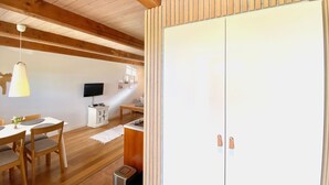 Ein Zimmer mit Holzbalken, einem Esstisch mit Stühlen, einem Fernseher und einem weißen Kleiderschrank.