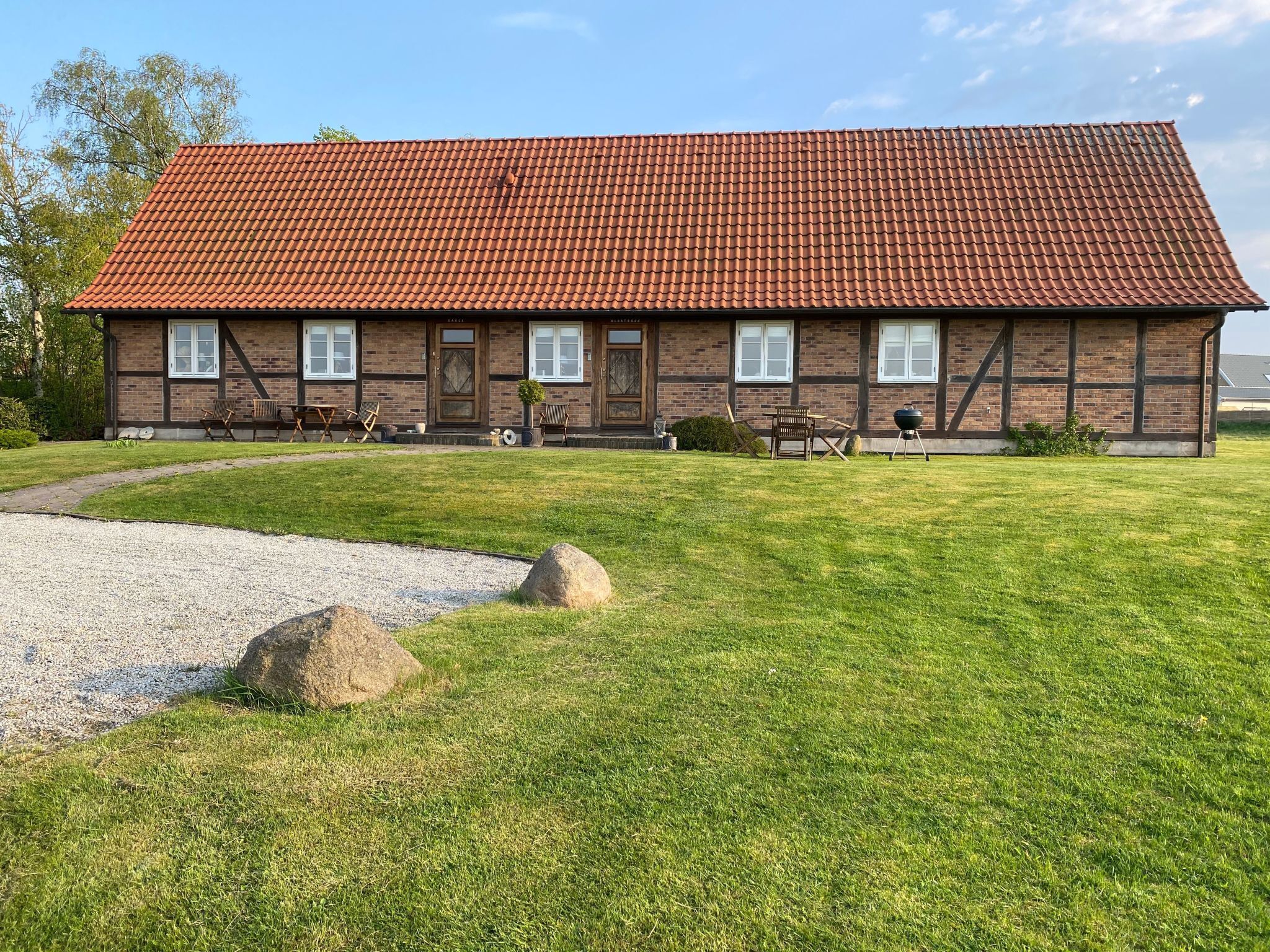 A two-story brick building with a red-tiled roof, a gravel driveway, and a grassy lawn with rocks.