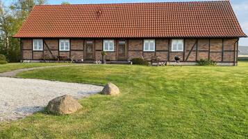 A two-story brick building with a red-tiled roof, a gravel driveway, and a grassy lawn with rocks.