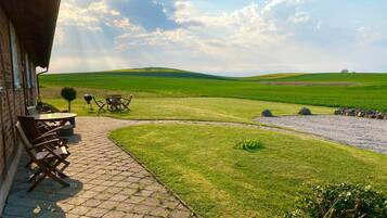 A patio with outdoor furniture, a stone pathway, and a view of a green field and hills.