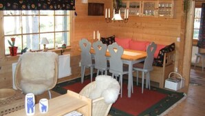 A cozy cabin interior with a wooden dining table, chairs, a sofa, and a fireplace.
