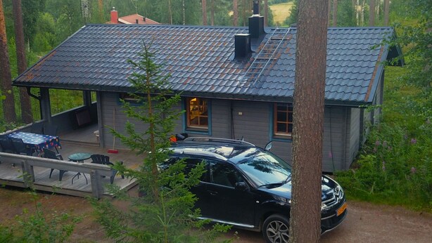 A cabin with a metal roof, a covered porch, and a car parked in front.