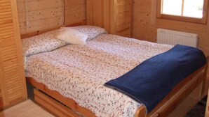 A wooden cabin bedroom with a bed, a window, and a radiator.