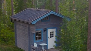 A small cabin with a blue roof and white door, surrounded by dense forest.