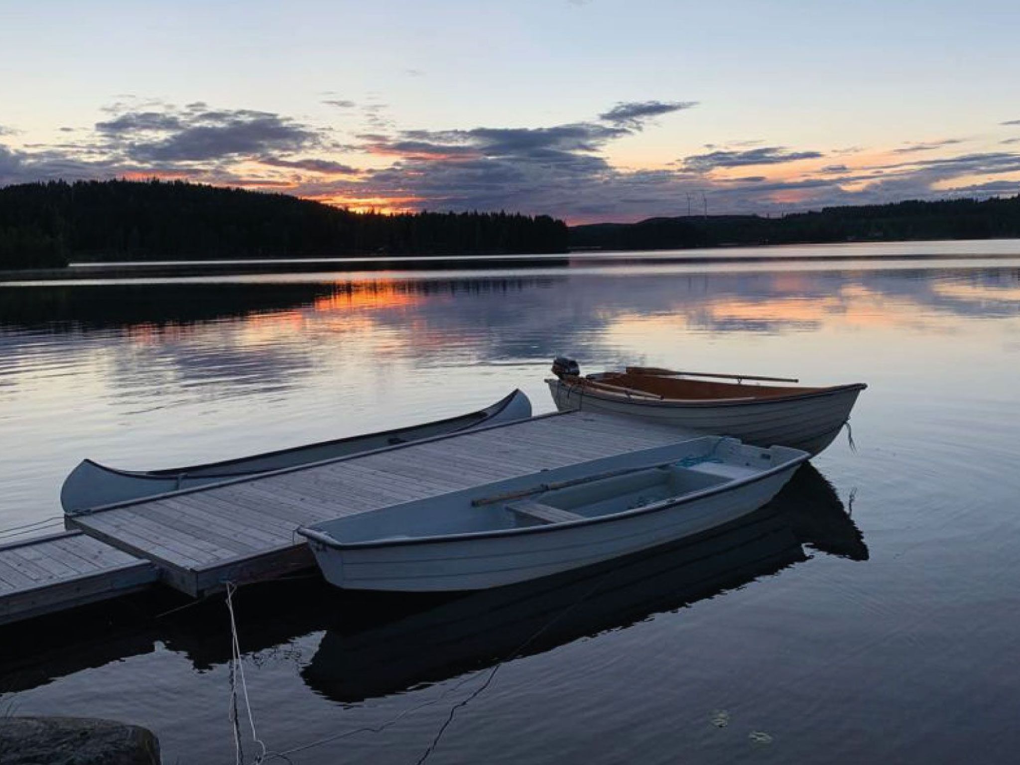 A calm lake at dusk with two boats docked at a wooden pier.