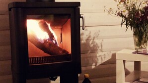 Un poêle à bois, avec des bûches et une bouteille de combustible, placé contre un mur en bois.