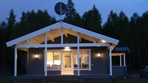 Une cabane moderne dotée d’un porche abrité, de grandes fenêtres et d’une antenne parabolique.
