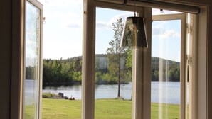 Une vue à travers une porte vitrée d’un lac, avec une zone herbeuse et des arbres en arrière-plan.