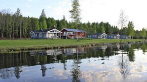 Une propriété au bord du lac comprenant plusieurs maisons, un quai et une étendue d’eau calme où se reflètent le ciel et les arbres.
