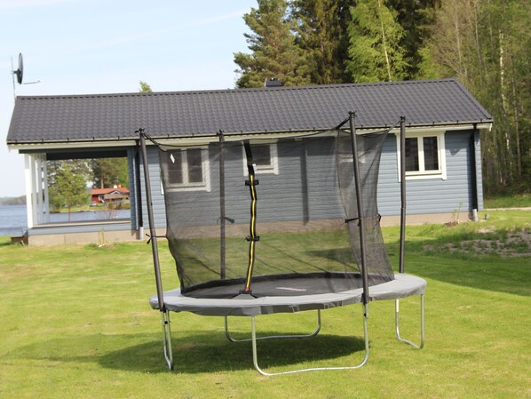 Un trampoline dans une cour verdoyante, avec une maison en arrière-plan.