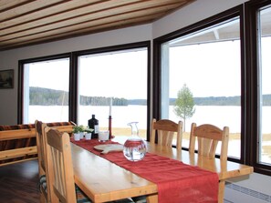 Un espace repas avec une table en bois, des chaises et une vue sur un lac, visible à travers de grandes fenêtres.