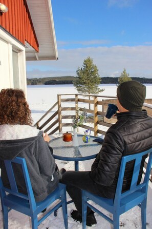 Dos personas sentadas en una mesa redonda de cristal, con vistas a un paisaje nevado con una valla de madera y un árbol.