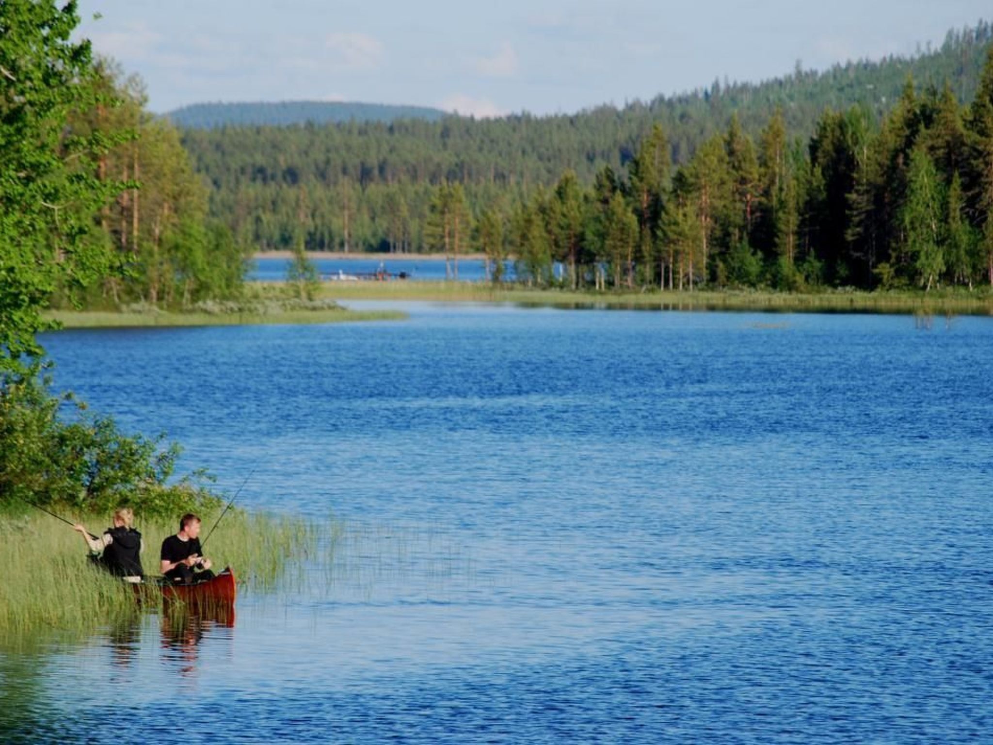 Ein ruhiger See mit zwei Personen in einem Kanu, umgeben von dichtem Wald und Hügeln im Hintergrund.