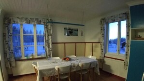 Un comedor con una mesa dispuesta para cuatro, una ventana que ofrece vistas a un paisaje nevado y un radiador debajo de la ventana.