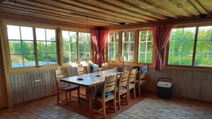 Zona pranzo con tavolo e sedie in legno, ampie finestre con tende e vista sul verde.