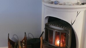 Una habitación con chimenea de ladrillo, una cesta de mimbre con leña y una pequeña mesa con un cuenco.