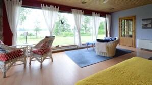 A room with a wooden ceiling, large windows with white curtains, wicker furniture, and a view of greenery outside. - Lilla Sjöbo by Interhome (Hok)