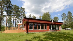 A red building with large windows, a covered deck, and a satellite dish. - Lilla Sjöbo by Interhome (Hok)