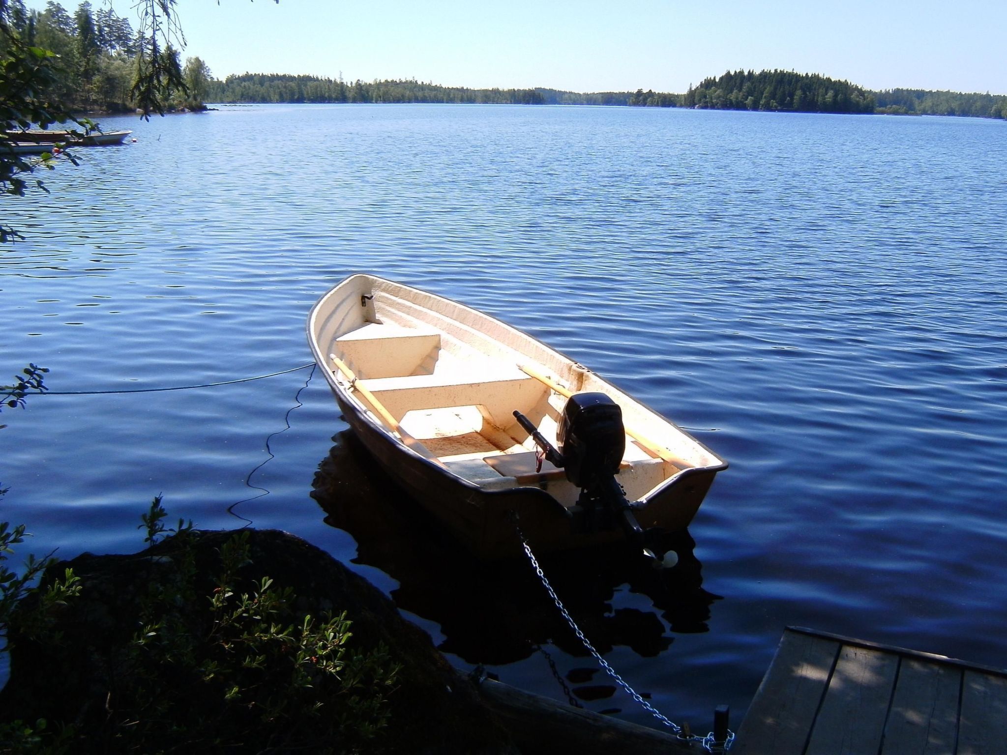 A small rowboat tied to a dock on a calm lake with forested shores in the background.