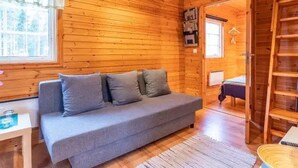 En mysig stuga med grå soffa, träväggar, ett litet bord och en stege.