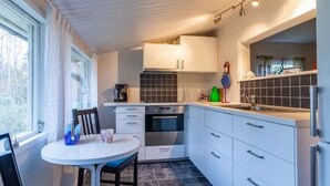 A compact kitchen with white cabinets, a black tiled backsplash, a round table with chairs, and a window providing natural light. - Gemütliches Ferienhaus in Seenähe by Interhome (Hallaryd)