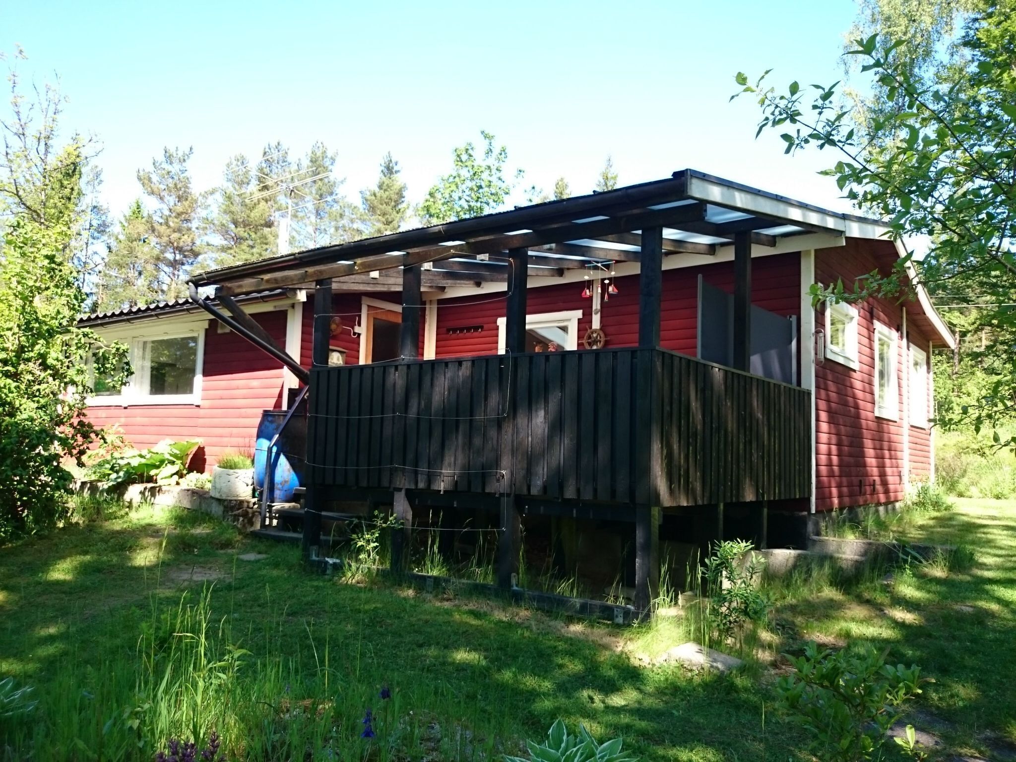 Ett rött trähus med en inglasad veranda och en liten trädgård.