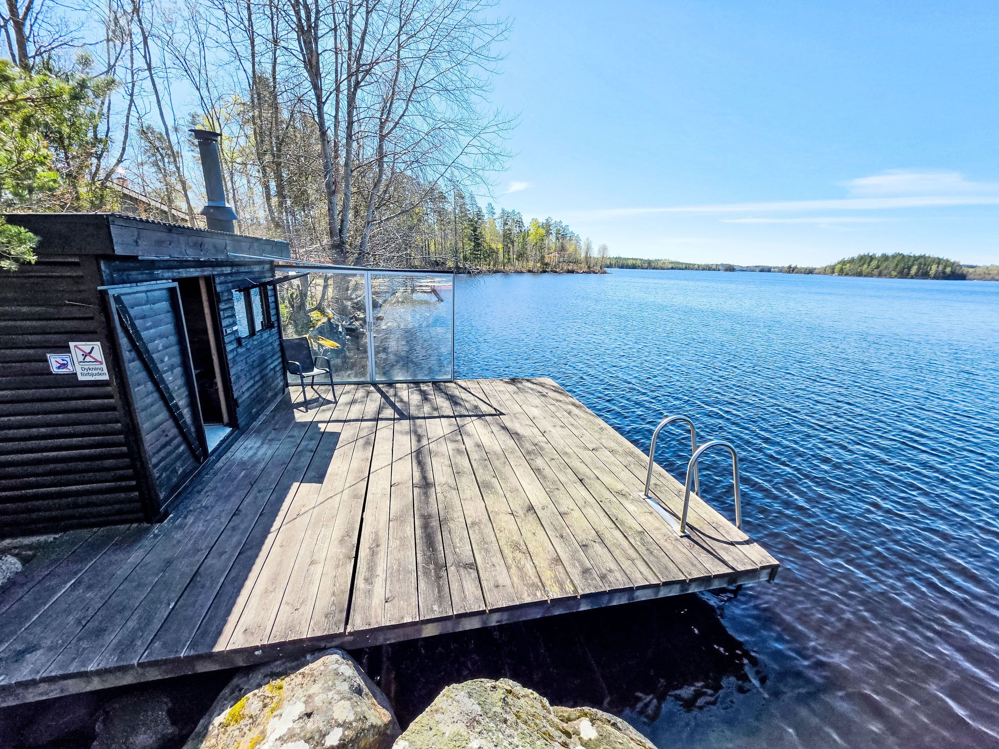A wooden dock extending into a calm lake, with a cabin on the left and a clear view of the water.