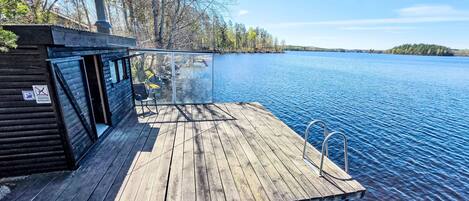 A wooden dock extending into a calm lake, with a cabin on the left and a clear view of the water.
