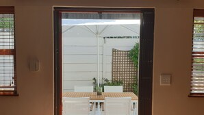 An open door leading to a patio area with a wooden table and white chairs. - in Kirstenhof mit Privatem Garten by Interhome (Kapstadt)