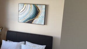 A hotel room with a bed, white pillows, and a wall-mounted abstract painting. - in Kirstenhof mit Privatem Garten by Interhome (Kapstadt)